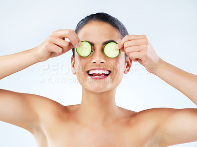 Buy stock photo Studio portrait of an attractive young woman covering her eyes with cucumbers against a gray background