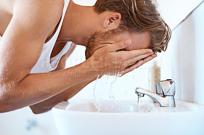 Buy stock photo Shot of a young man washing his face at a basin in the bathroom