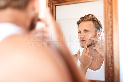 Buy stock photo Shot of a young man examining his skin in the mirror at home
