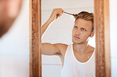 Buy stock photo Shot of a young man looking at his hair in the mirror at home