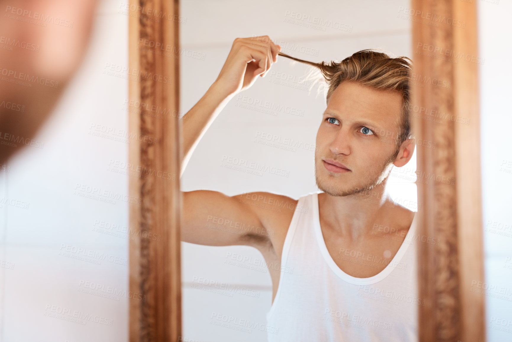 Buy stock photo Shot of a young man looking at his hair in the mirror at home