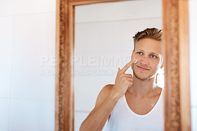 Buy stock photo Shot of a young man applying moisturizer to his face at home