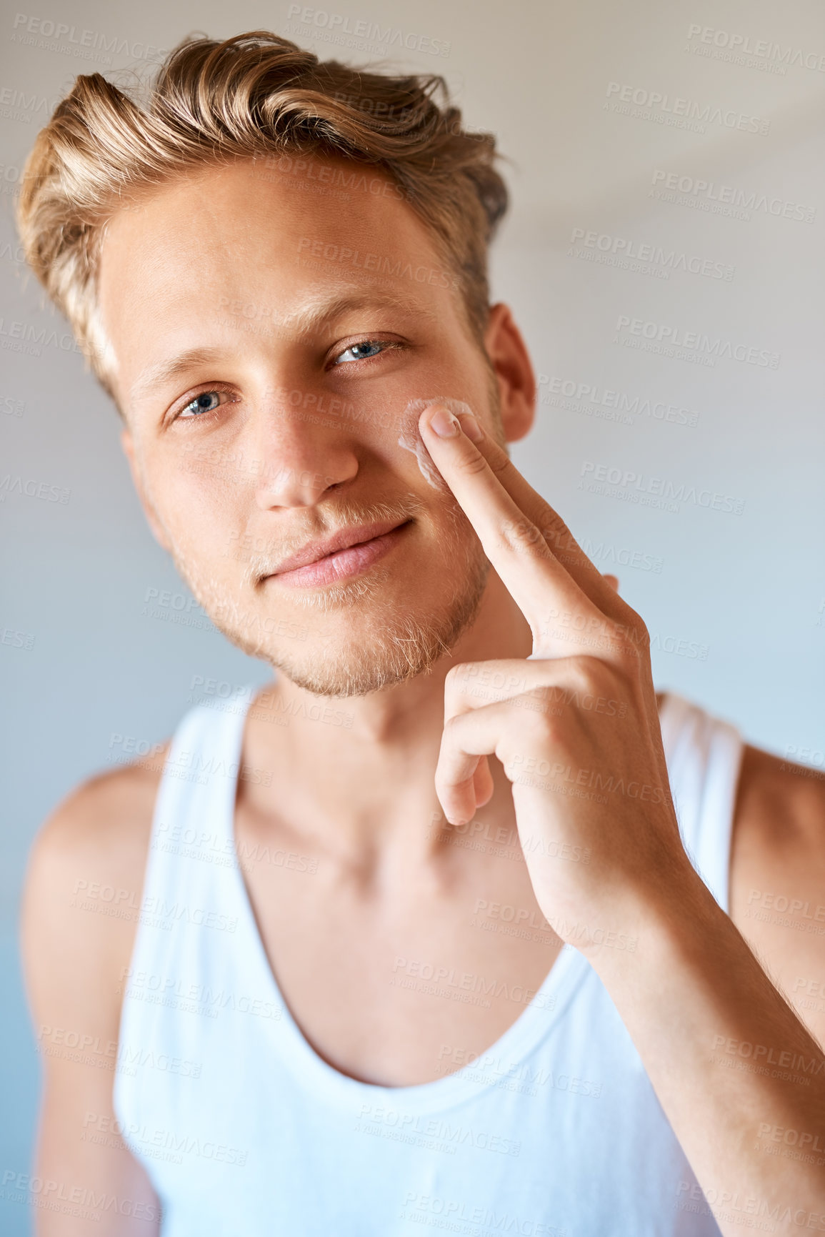 Buy stock photo Portrait of a young man applying moisturizer to his face at home