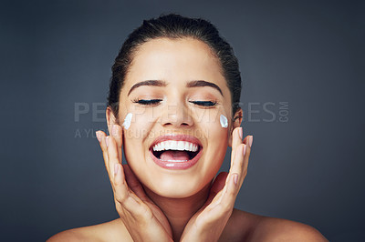 Buy stock photo Studio shot of a beautiful young woman with moisturizer on her face while posing against a blue background