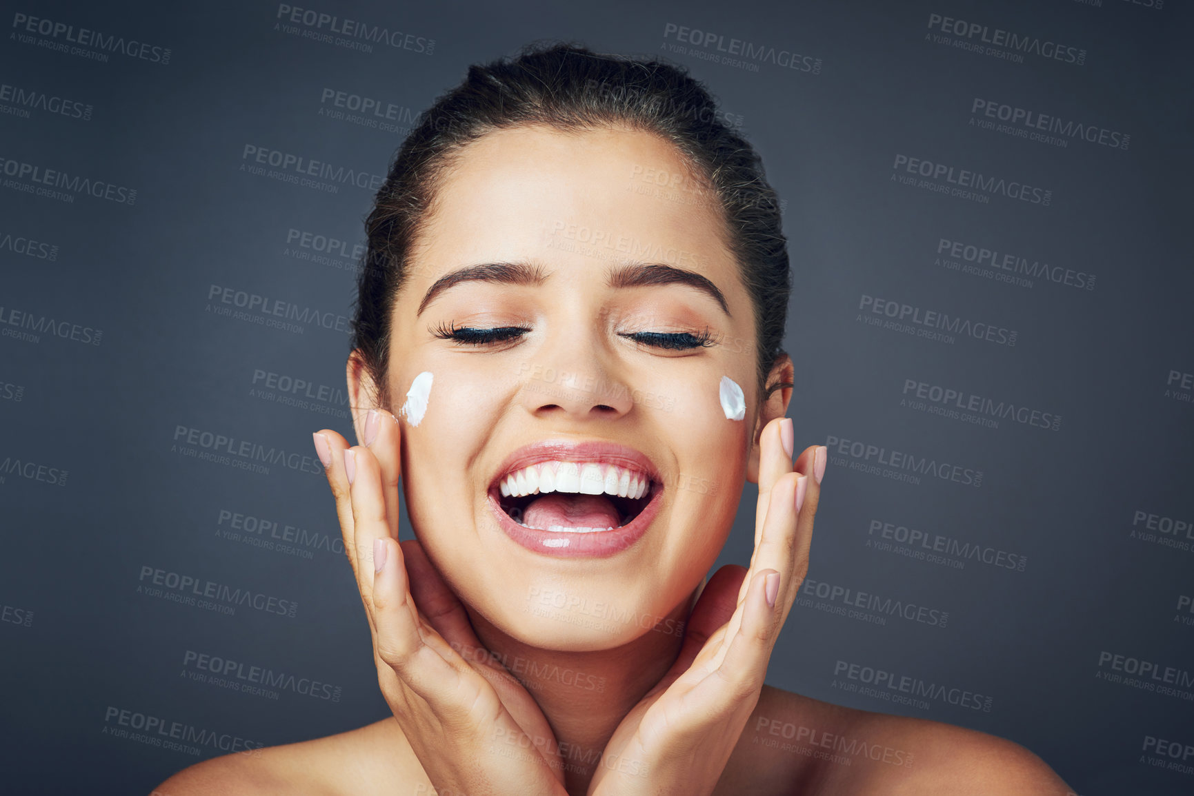 Buy stock photo Studio shot of a beautiful young woman with moisturizer on her face while posing against a blue background