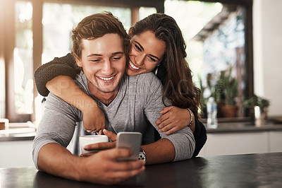 Buy stock photo Shot of an affectionate young couple using a mobile phone on a coffee break at home