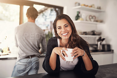 Buy stock photo Portrait of a young woman having coffee in the kitchen with her husband standing in the background