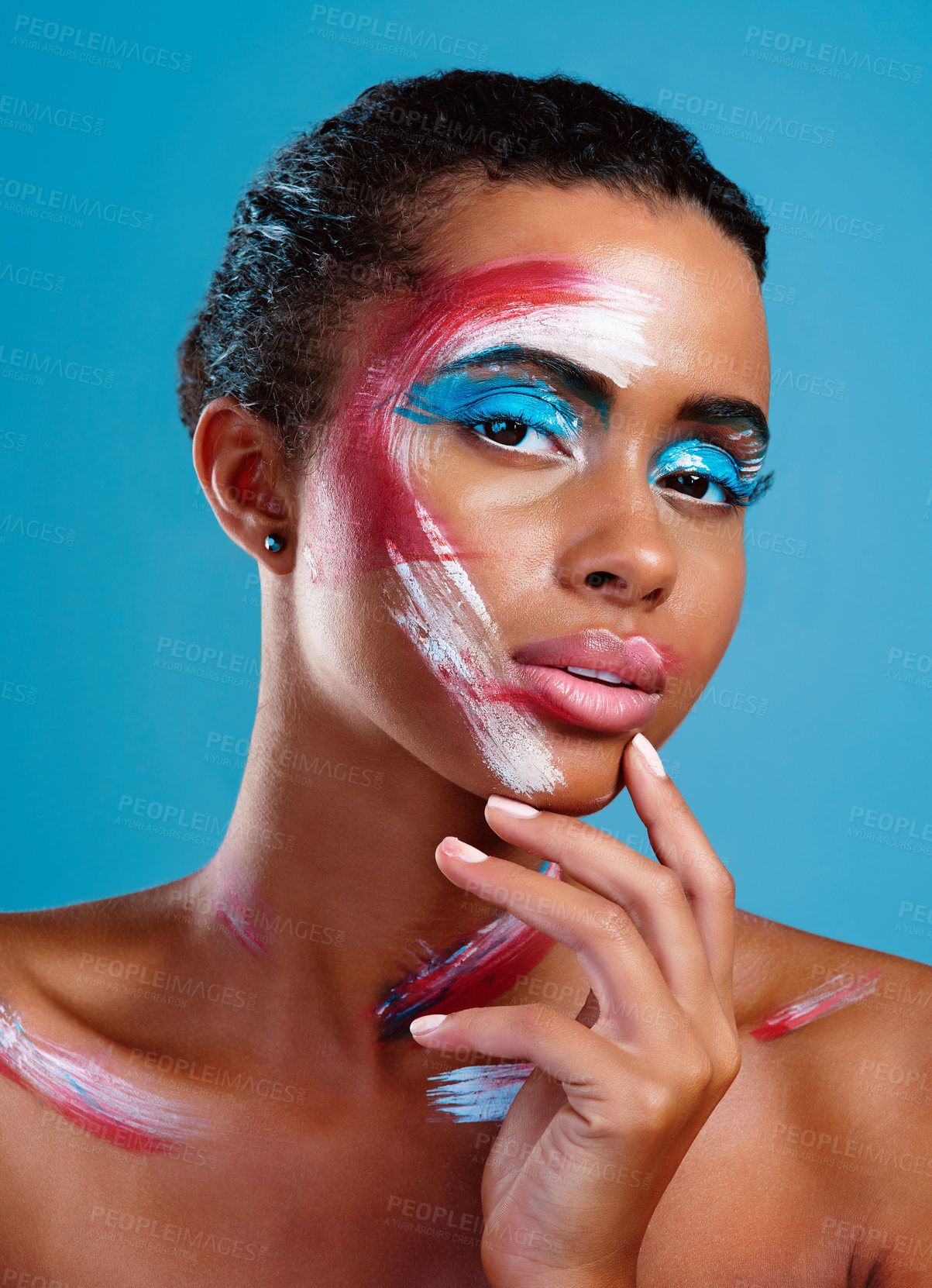 Buy stock photo Studio portrait of a beautiful young woman covered in face paint posing against a blue background