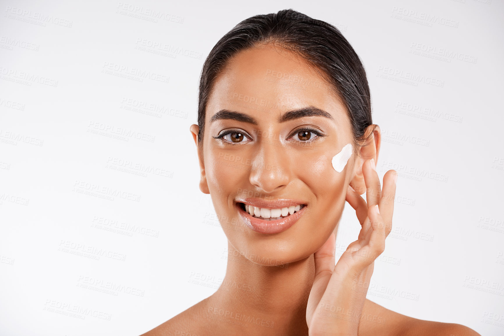 Buy stock photo Studio portrait of a beautiful young woman applying lotion while posing against a gray background