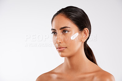 Buy stock photo Studio shot of a beautiful young woman posing with lotion on her face against a gray background