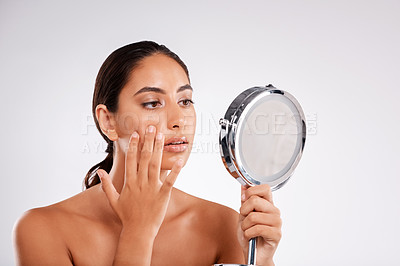 Buy stock photo Studio shot of a beautiful young woman examining her skin in a handheld mirror against a gray background