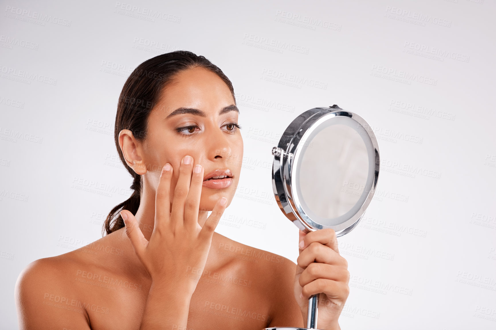 Buy stock photo Studio shot of a beautiful young woman examining her skin in a handheld mirror against a gray background