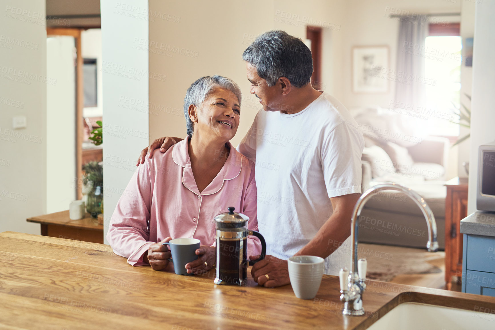 Buy stock photo Shot of a cheerful elderly couple holding each other while looking into each other's eyes and drinking coffee at home during the day