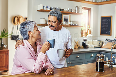 Buy stock photo Shot of a cheerful elderly couple holding each other while looking into each other's eyes and drinking coffee at home during the day