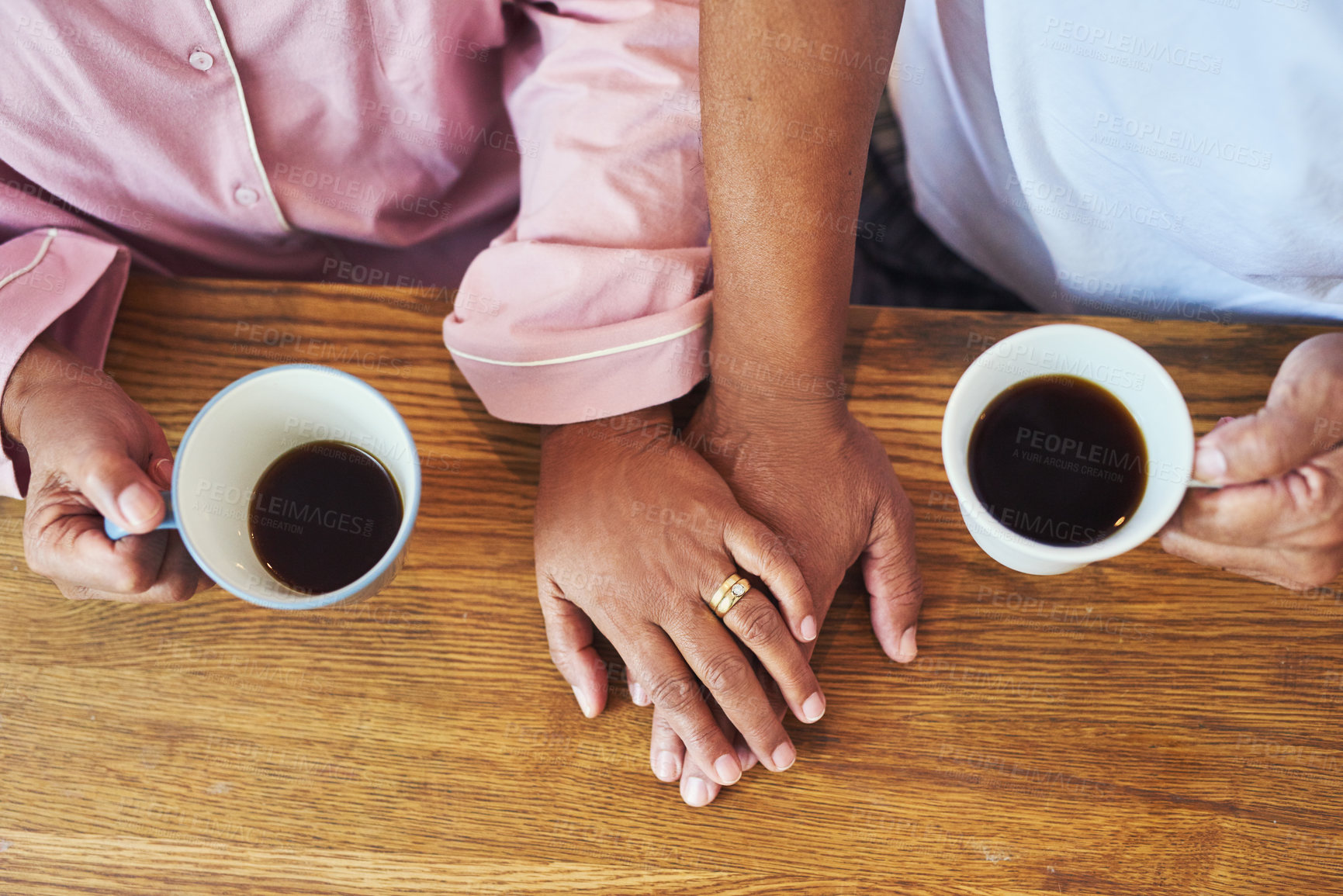 Buy stock photo High angle closeup of an unrecognizable couple holding hands while drinking coffee on a table at home during the day