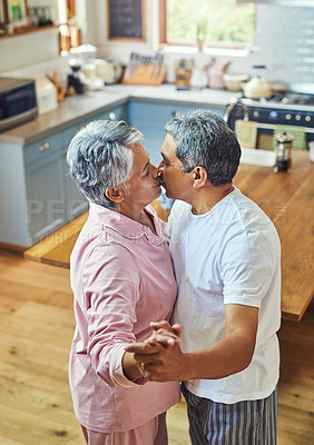 Buy stock photo Shot of a carefree elderly couple having a dance while sharing a kiss inside of the kitchen at home during the day