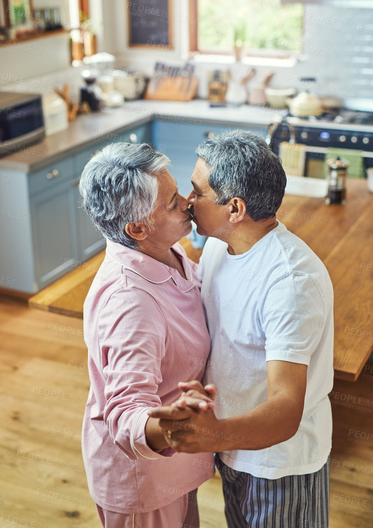 Buy stock photo Shot of a carefree elderly couple having a dance while sharing a kiss inside of the kitchen at home during the day
