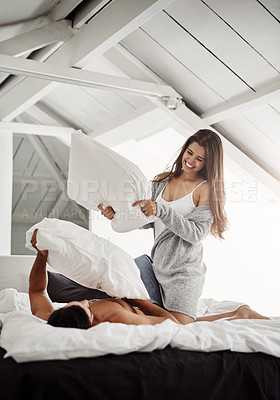 Buy stock photo Shot of a young couple having a pillow fight in their bedroom at home
