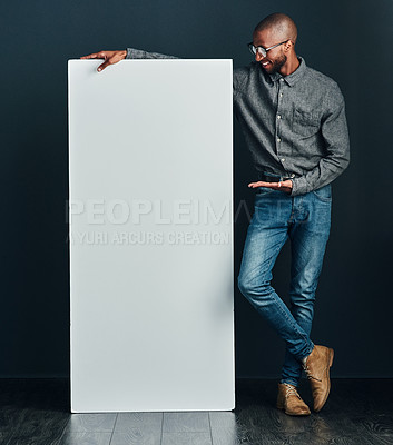 Buy stock photo Shot of a handsome young man standing next to a blank placard