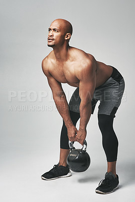 Buy stock photo Studio shot of an athletic young man working out with a kettle bell against a grey background