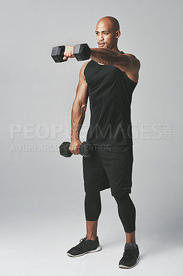 Buy stock photo Studio shot of an athletic young man working out with dumbbells against a grey background