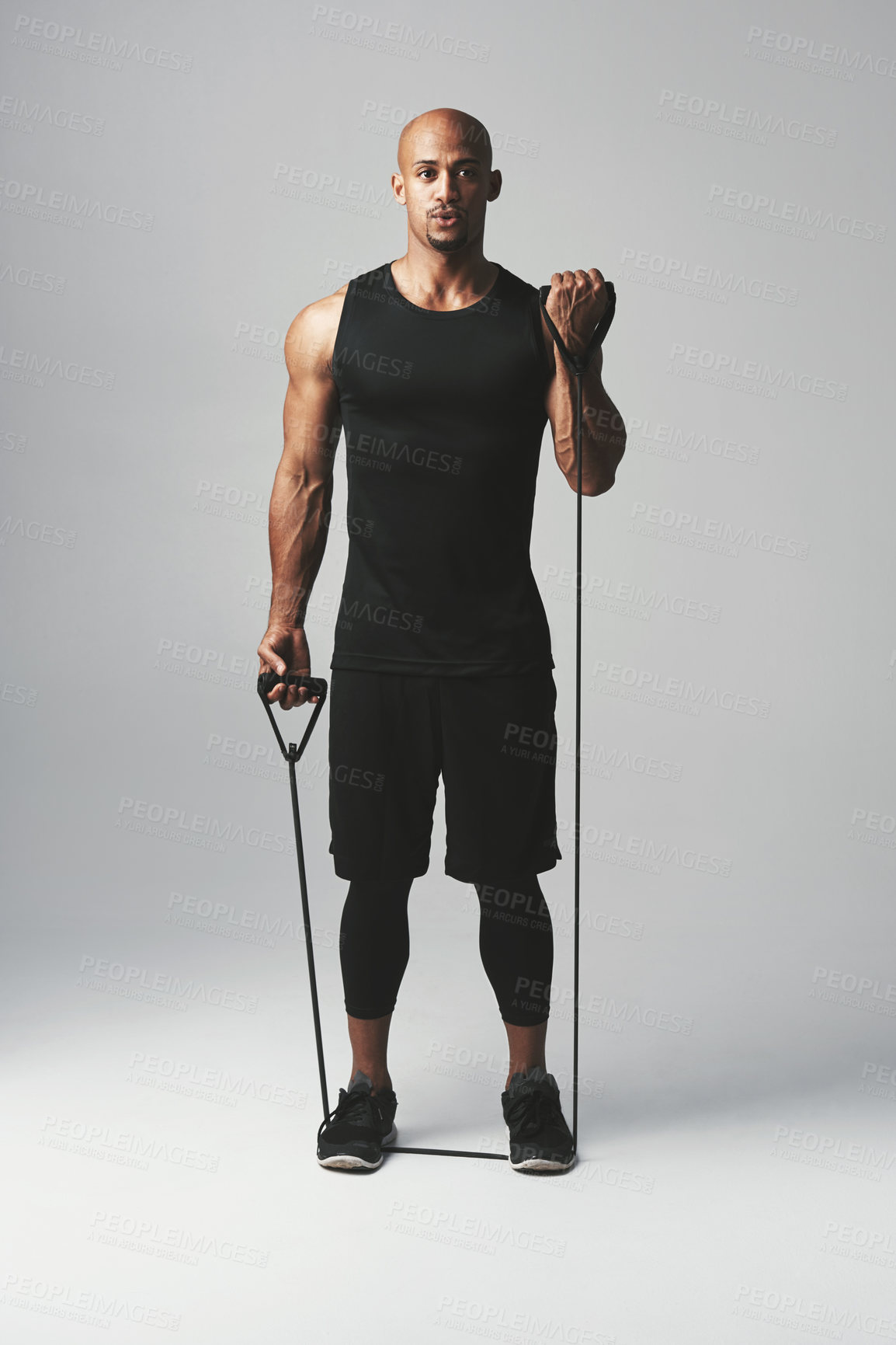 Buy stock photo Studio portrait of an athletic young man working out with a resistance band against a grey background