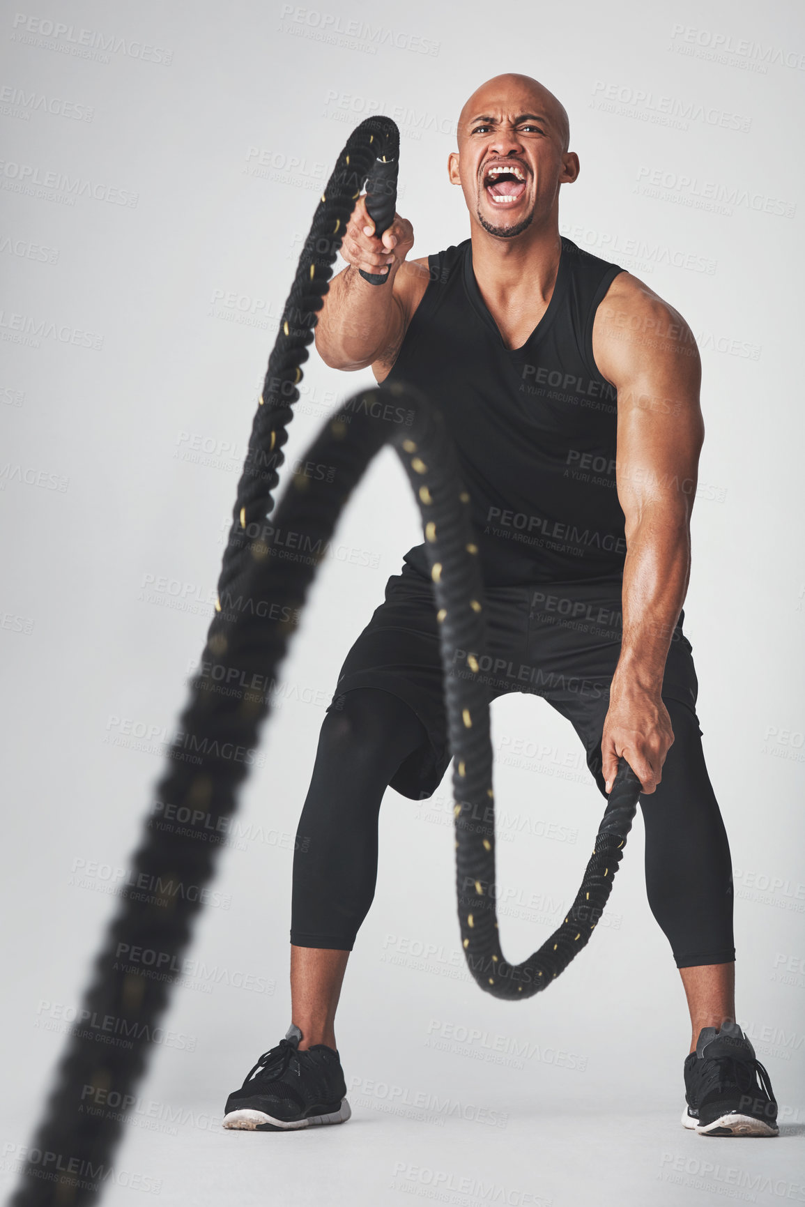 Buy stock photo Studio shot of an athletic young man working out with battle ropes against a grey background