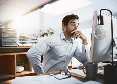 Buy stock photo Shot of a young businessman looking stressed out while working late on a computer in an office