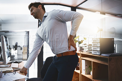 Buy stock photo Shot of a young businessman suffering with back pain while working late in an office