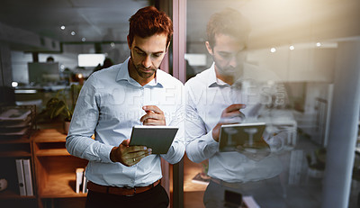 Buy stock photo Shot of a young businessman working late on a digital tablet in an office