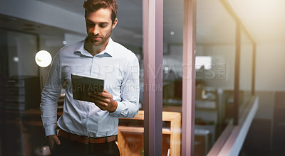 Buy stock photo Shot of a young businessman working late on a digital tablet in an office
