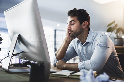 Buy stock photo Shot of a young businessman looking exhausted while working late on a computer in an office