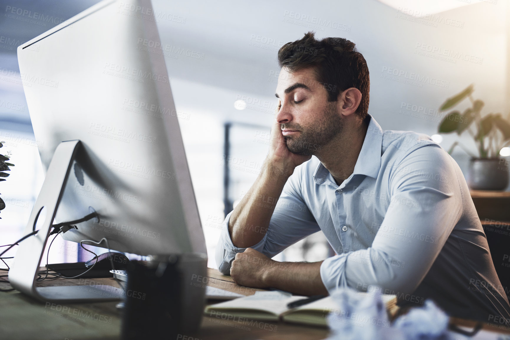 Buy stock photo Shot of a young businessman looking exhausted while working late on a computer in an office