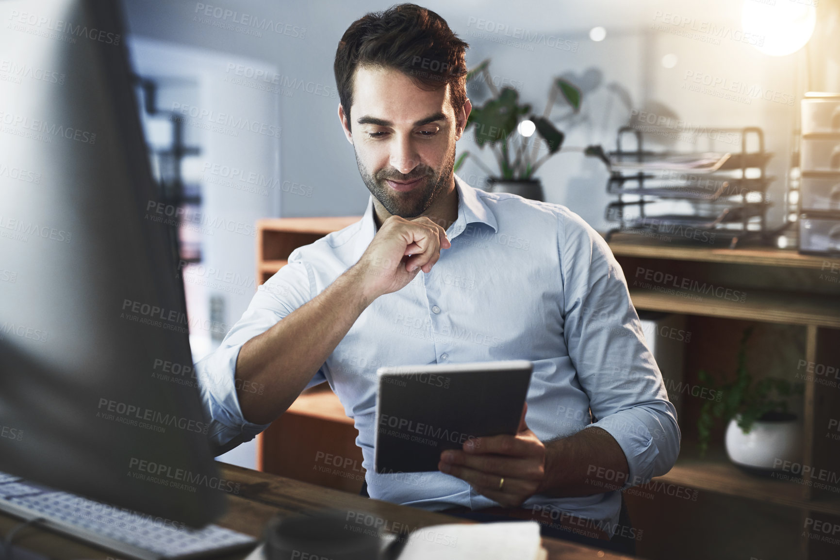 Buy stock photo Shot of a young businessman working late on a digital tablet in an office