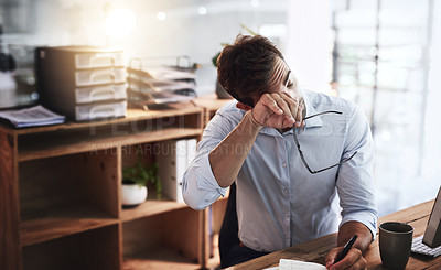 Buy stock photo Shot of a young businessman looking exhausted while working late in an office