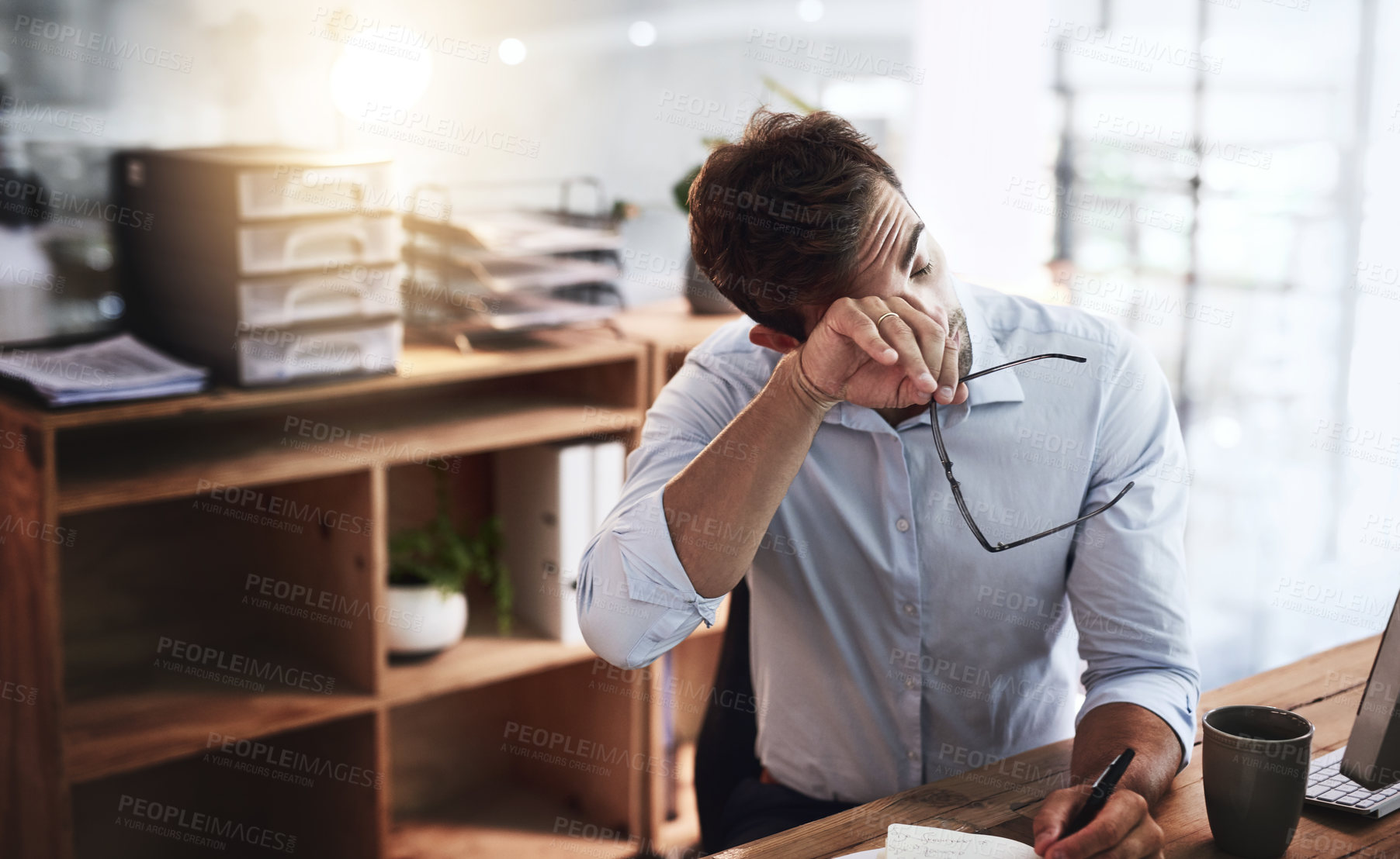 Buy stock photo Shot of a young businessman looking exhausted while working late in an office