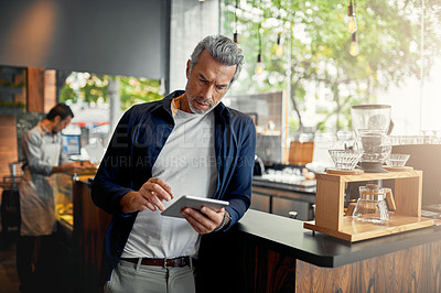 Buy stock photo Cropped shot of a handsome mature man working on a digital tablet while standing in his coffee shop