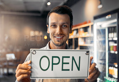 Buy stock photo Cropped portrait of a handsome young man holding up an open sign while standing in his coffee shop
