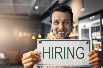 Buy stock photo Cropped portrait of a handsome young man holding up a hiring sign while standing in his coffee shop
