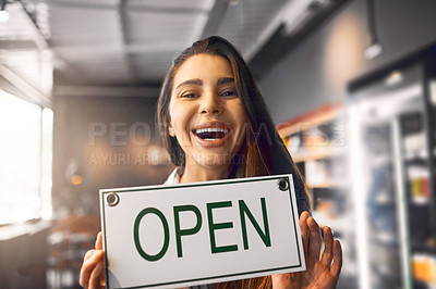 Buy stock photo Cropped portrait of an attractive young woman holding up an open sign while standing in her coffee shop
