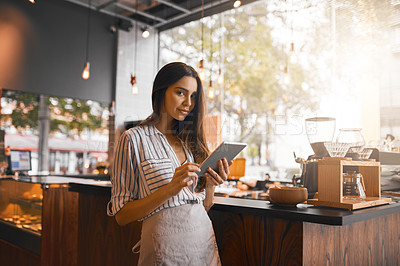 Buy stock photo Cropped portrait of an attractive young woman working on a digital tablet while standing in her coffee shop