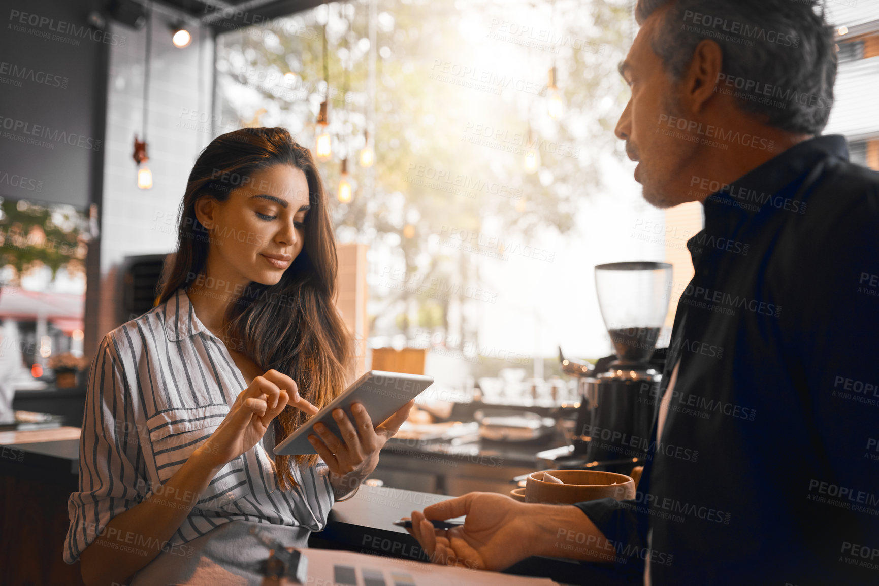 Buy stock photo Cropped shot of an attractive young woman processing a male customer's payment on her tablet while working in her coffee shop