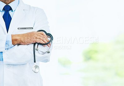Buy stock photo Cropped shot of an unrecognizable male doctor standing with his arms folded inside of a hospital during the day