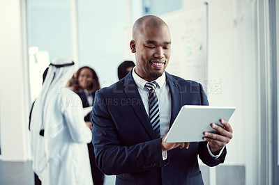 Buy stock photo Cropped shot of a handsome young businessman working on a tablet in the office with his colleagues in the background