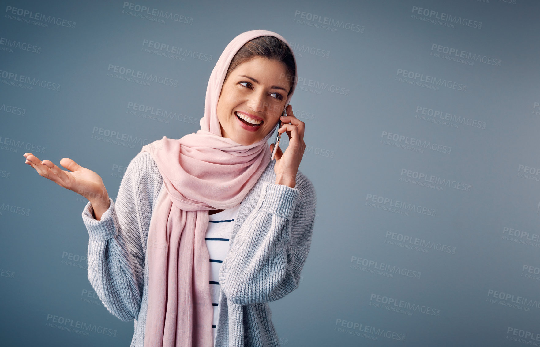 Buy stock photo Talking, phone call and muslim woman with smartphone in studio for conversation, networking or gossip on blue background. Contact, happy and Arab person with for chatting,  speaking or discussion 