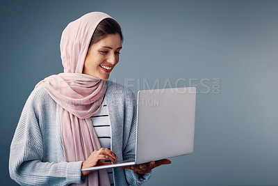 Buy stock photo Studio shot of an attractive young woman using her laptop while standing against a grey background