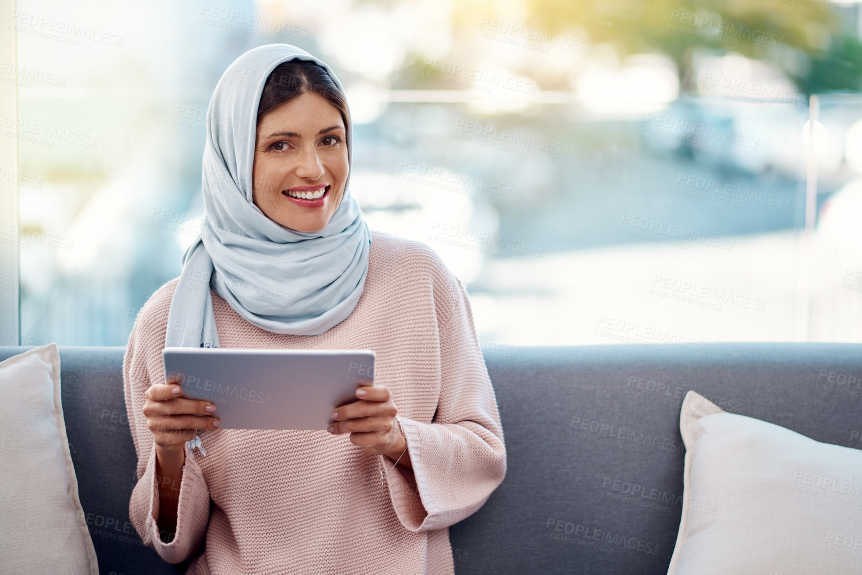 Buy stock photo Cropped portrait of an attractive young woman using her tablet while chilling on her sofa at home