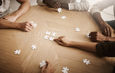Buy stock photo Friends hands solving a puzzle in a group collaboration together as a team on wooden table indoors. Diverse colleagues using teamwork and support to help each other to find a smart solution close up