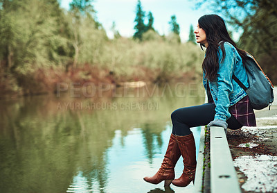 Buy stock photo Shot of a young woman sitting by a lake outdoors