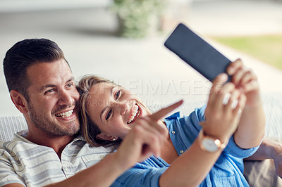 Buy stock photo Cropped shot of a young married couple taking a selfie using a cellphone on the sofa at home